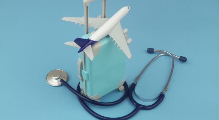 Airplane on suitcase and stethoscope on blue background. Travel insurance, medical tourism, health care concept.