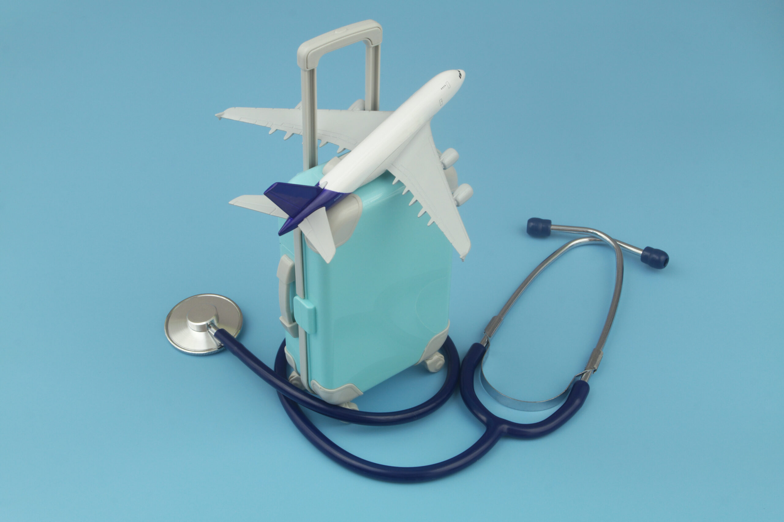 Airplane on suitcase and stethoscope on blue background. Travel insurance, medical tourism, health care concept.