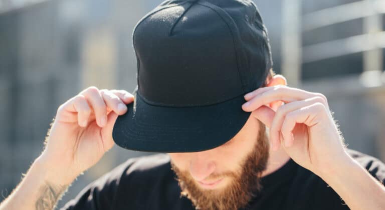 Man placing a black baseball cap on his head.