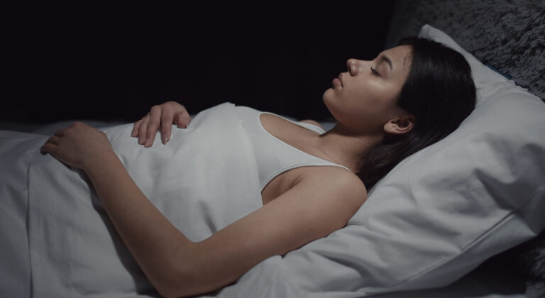 Brunette woman sleeping on her back in white cotton sheets.