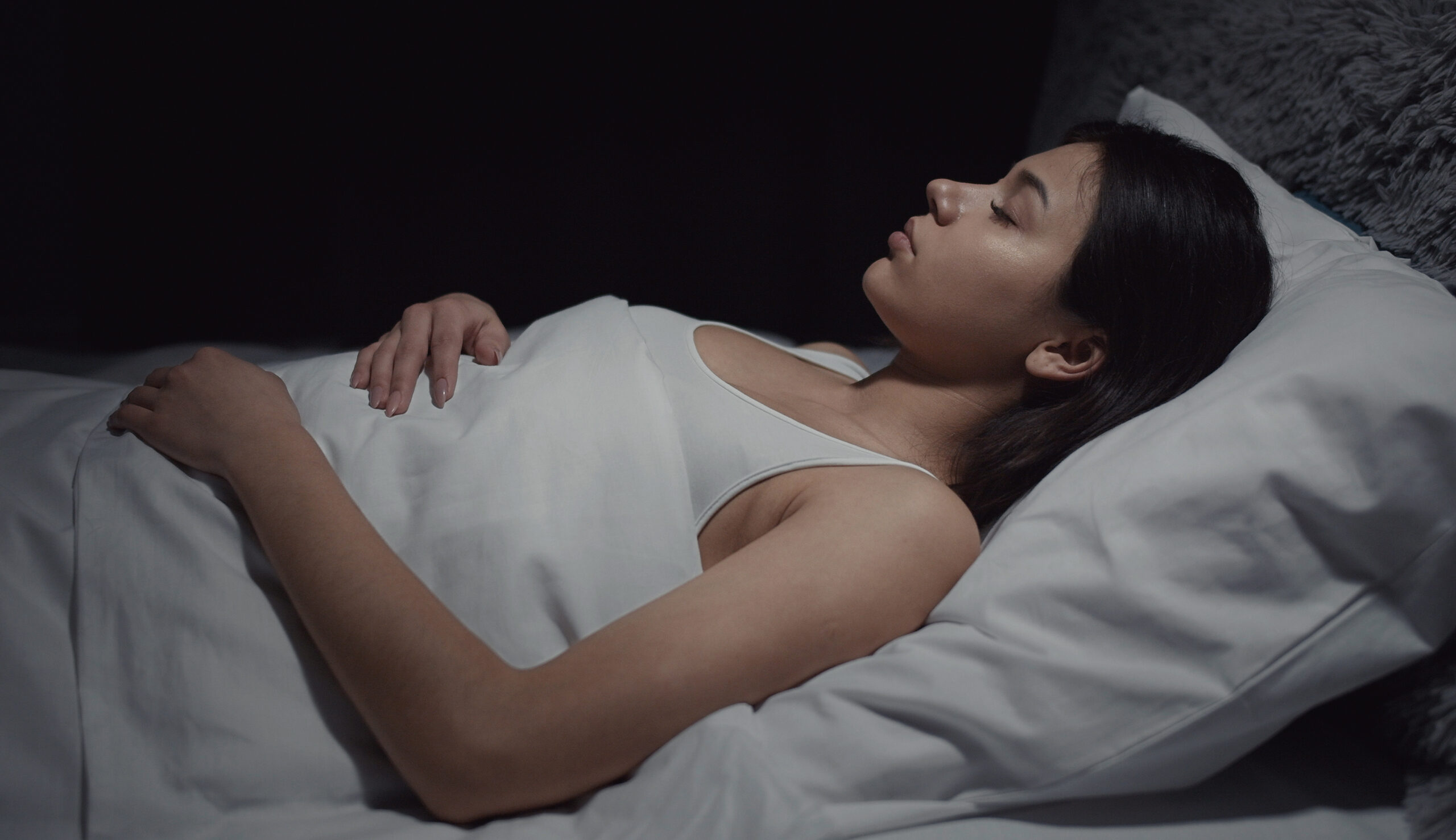 Brunette woman sleeping on her back in white cotton sheets.