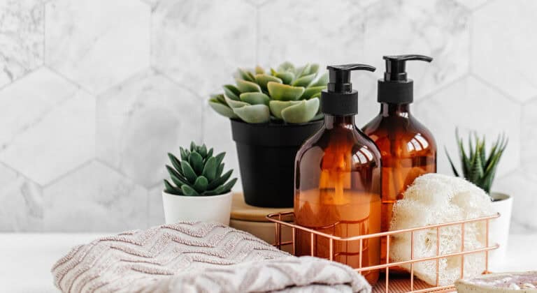 Soap and shampoo bottles and cotton towels with green plant on white table inside a bathroom background.