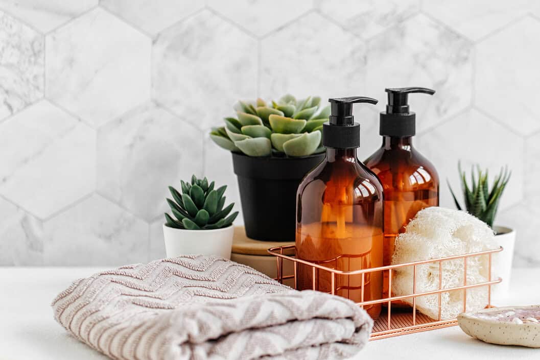 Soap and shampoo bottles and cotton towels with green plant on white table inside a bathroom background.