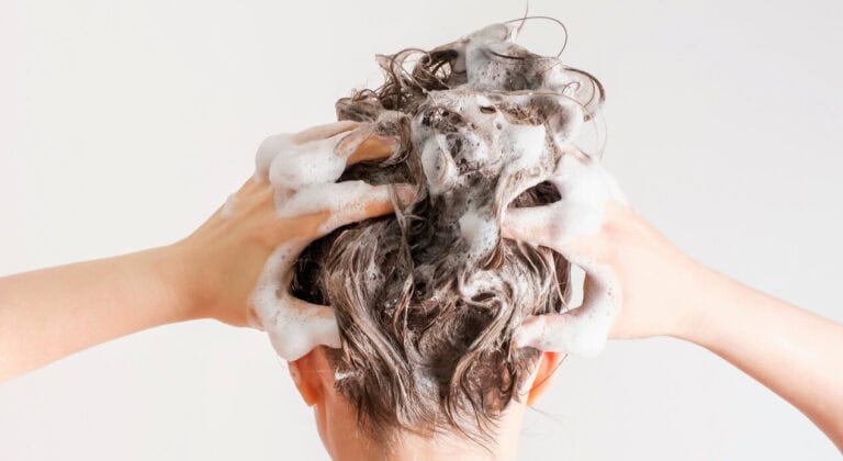 A girl washes her hair with shampoo on white background, back view.