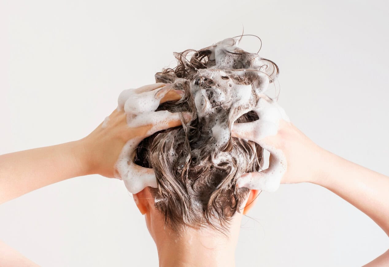 A girl washes her hair with shampoo on white background, back view.